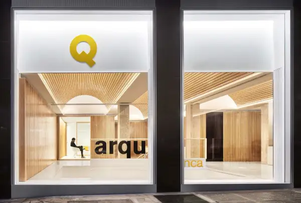 Interior de una oficina de arquitectos con paredes de madera, techo curvo y el logo "Q" en amarillo.